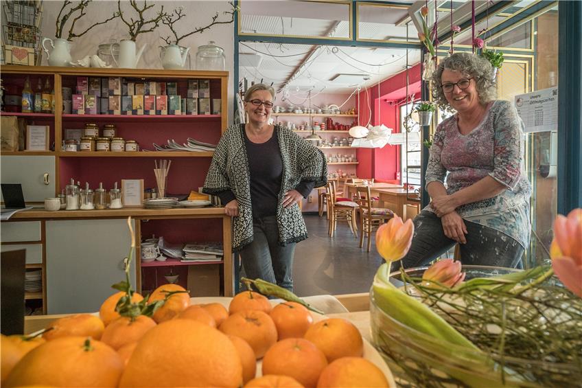 Vorne leuchten Orangen, an der hinteren Wand stehen bunte Gedecke. Dazwischen die Cafébetreiberinnen Margrit Götz (links) und Petra Kühne. Bild: Metz