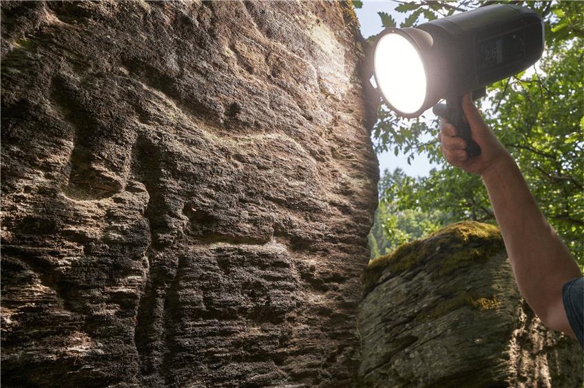 Der Archäologe Wolfgang Welker macht mit einer Lampe die Felsgravuren sichtbar. Foto: Thomas Frey/dpa