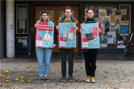 Die Studierenden Helene Merz, Jacob Bühler und Johanna Grün (von links) mit Plakaten, die auf das Notlagenstipendium aufmerksam machen, vor dem Clubhaus.Bild: Carolin Albers