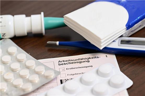 Ein Fieberthermometer, Medikamente und eine ärztliche Arbeitsunfähigkeitsbescheinigung (Krankmeldung) liegen auf einem Nachttisch. Foto: Bernd Weißbrod/dpa/Symbolbild