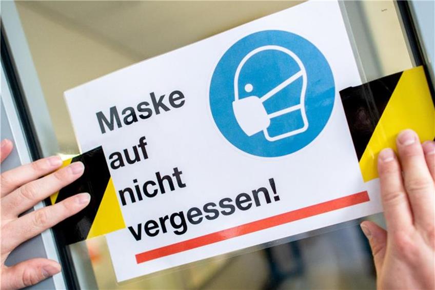 Ein Hausmeister bringt in der Schule ein Hinweisschild zum Tragen einer Maske an. Symbolbild: Hauke-Christian Dittrich/dpa