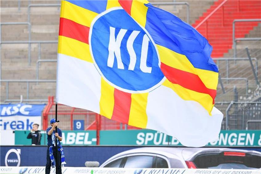 Ein Karlsruher Fan schwenkt vor Spielbeginn vor leeren Zuschauerrängen eine Fahne mit der Aufschrift "KSC". Foto: Uwe Anspach/Archiv
