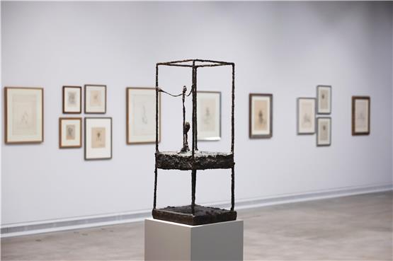 Ein Mensch in seinem Käfig: Alberto Giacomettis bekanntes Werk „La cage“ aus dem Jahr 1950 vor einer Wand mit Porträtzeichnungen im Kunstmuseum Ravensburg. Foto: Wynrich Zlomke
