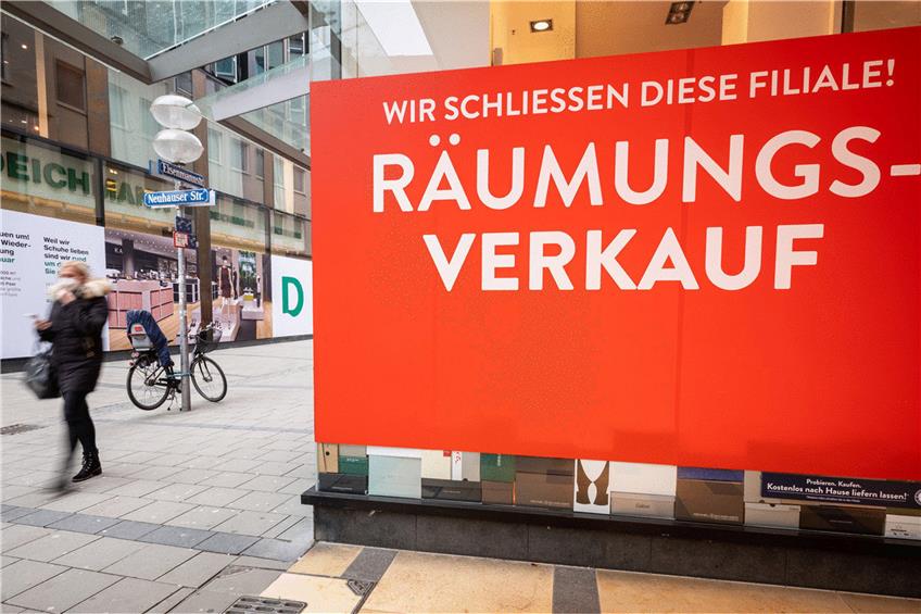 Ein Passantin läuft durch die fast leere Münchner Innenstadt an einem Geschäft vorbei, an dem das ein Schild mit der Aufschrift "Wir schliessen diese Filiale! - Räumungsverkauf" im Schaufenster an die Fensterscheibe geklebt wurde. Foto: Peter Kneffel/dpa