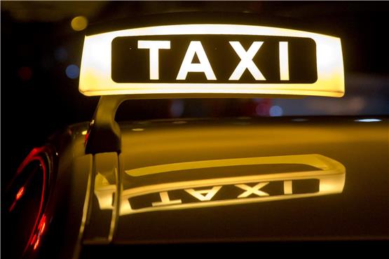 Ein beleuchtetes Taxi-Schild auf einem Autodach. Foto: Daniel Karmann/dpa/Archivbild