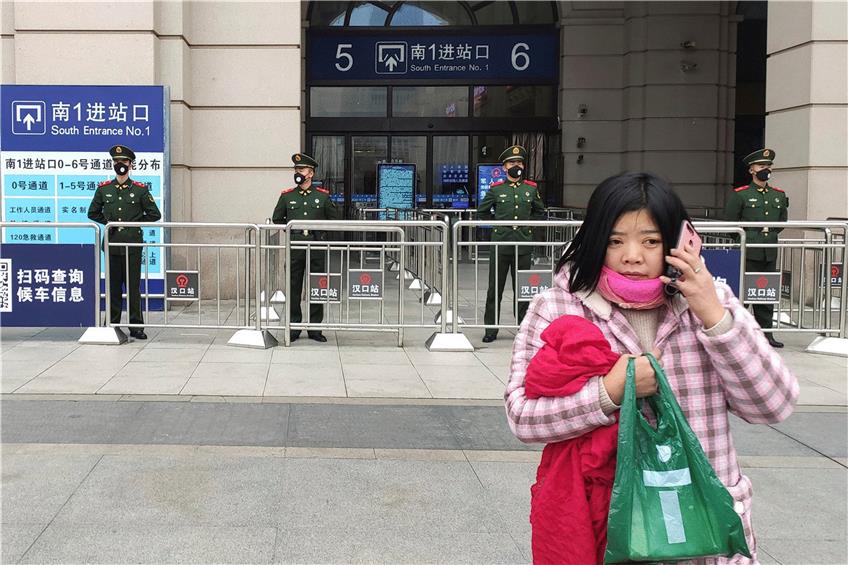 Eine Frau telefoniert, während paramilitärische Polizei einen Eingang zum Bahnhof Hankou in Wuhan abriegelt. Foto: --/Thepaper/AP/dpa