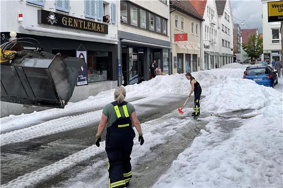 Einsatzkräfte der Feuerwehr räumen Hagel von einer Straße. Winterdienst-Einsatz mitten im Sommer 2023: Ein lokal begrenztes Unwetter hat Straßen in der Innenstadt von Reutlingen mit einer hohen Hagel-Schicht überzogen. Foto: Schulz/SDMG/dpa