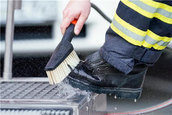 Kontaminierte Einsatzmaterialien: Ein Feuerwehrmann säubert an einer Stiefelwäsche seine Schuhe.  Foto: Uwe Anspach/dpa