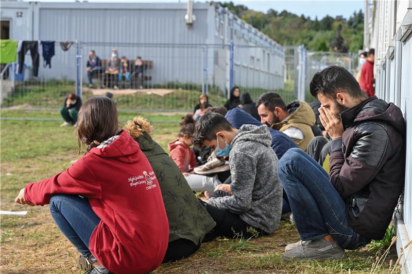 Mehrere Migranten sitzen auf einer Wiese vor Containern in der Zentralen Erstaufnahmeeinrichtung für Asylbewerber (ZABH) des Landes Brandenburg in Eisenhüttenstadt. Der Zustrom aus Richtung Polen wächst. Foto: Patrick Pleul