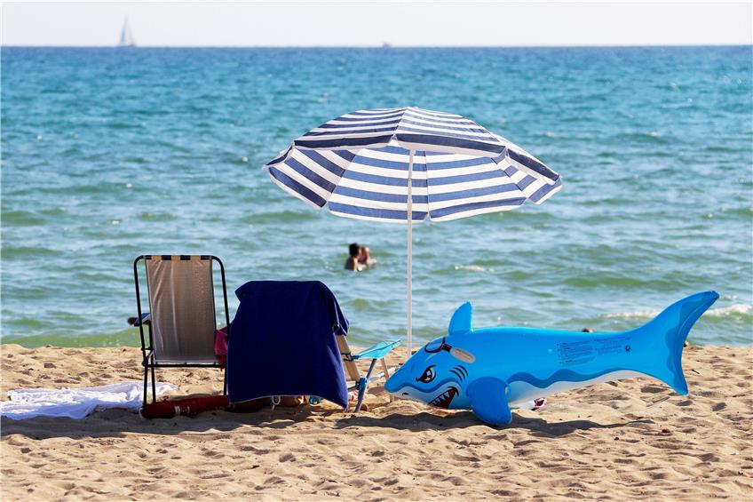 Mit Sonnenschirm und aufblasbaren Hai am Strand liegen? Davon träumen derzeit vermutlich einige Menschen. Bil: Clara Margais/dpa