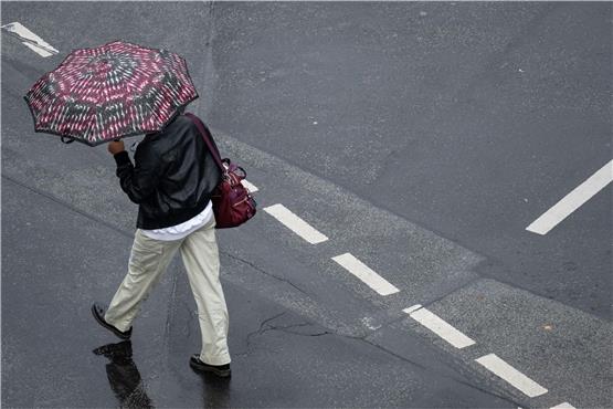 Mit einem Schirm schützt sich eine Passantin vor dem strömenden Regen. Foto: Boris Roessler/dpa/Symbolbild