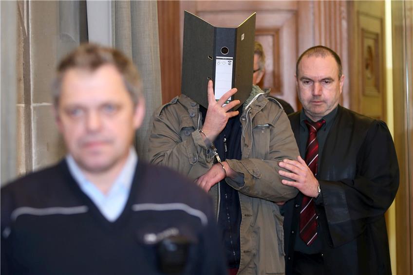 Verteidiger Andreas Eggstein (rechts) führt den Angeklagten, der sein Gesicht hinter einem Aktenordner versteckt, in den Schwurgerichtssaal. Links im Vordergrund ein Justizbeamter. Bild: dpa