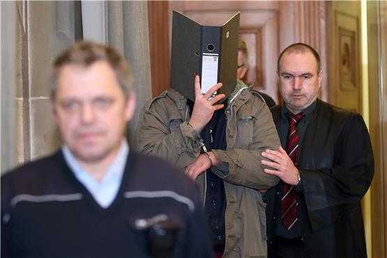 Verteidiger Andreas Eggstein (rechts) führt den Angeklagten, der sein Gesicht hinter einem Aktenordner versteckt, in den Schwurgerichtssaal. Links im Vordergrund ein Justizbeamter. Bild: dpa